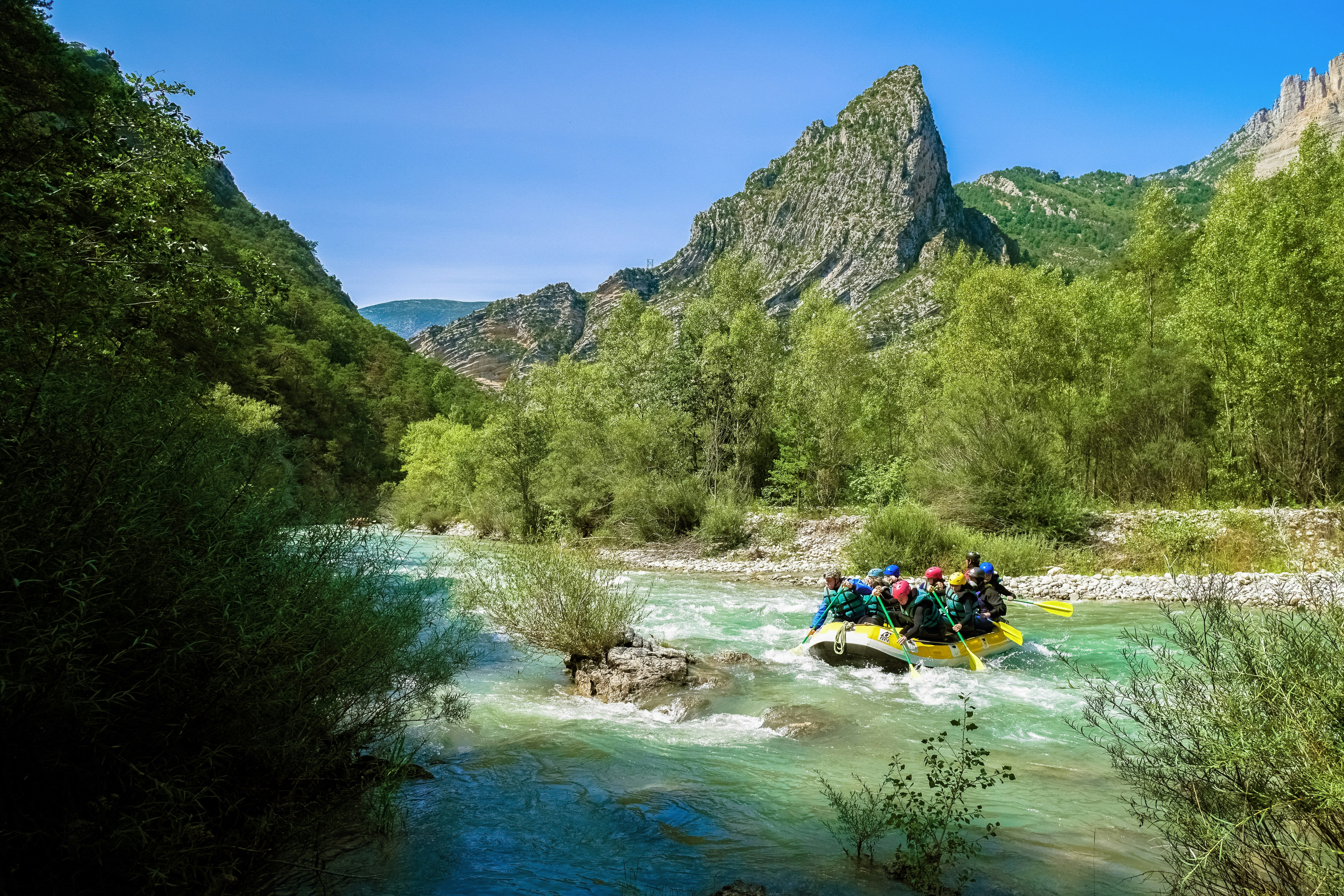 people riding on yellow kayak on river near green trees and mountain during daytime